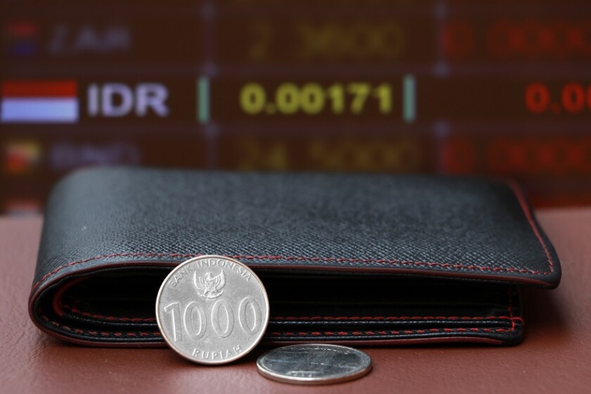 Two coins of one thousand Indonesia Rupiah money and black leather wallet on brown floor with digital board of currency exchange background.
