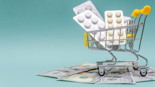 yellow shopping cart with pills stands on dollar bills on a blue background close-up. Concept of healthcare, online shopping, high cost of medicines. Copy space