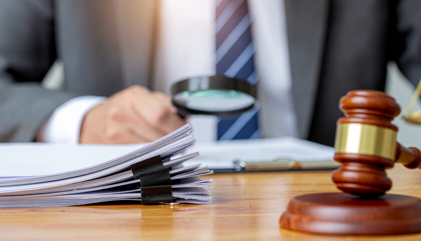 Professional reviewing legal paperwork with magnifying glass next to a judge gavel