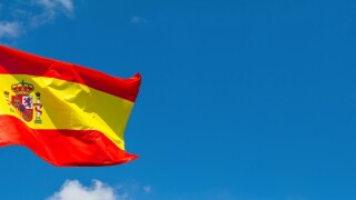 Flag of Spain waving in the wind on flagpole against the sky with clouds on sunny day, banner