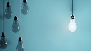 Hanging light bulbs on blue background with one illuminated and space for text