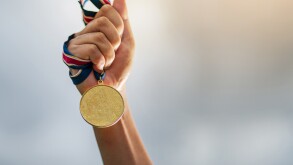 Hand holding gold medal on sky background