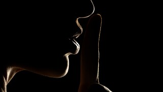 Silhouette of unknown woman , face in the shadow holding finger on her lips on a black background