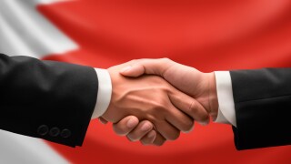 Businessman, diplomat in suits clasp hands for handshake over Bahrain flag, agree on united success in trade, diplomacy, cooperation, negotiation, support, teamwork in commerce, gesture of greeting