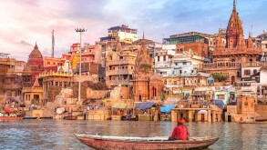 Ancient Varanasi city architecture at sunset with view of sadhu baba enjoying a boat ride on river Ganges.
