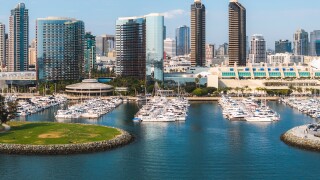 Aerial view of San Diego, California, featuring a skyline of high rise buildings, a marina with boats, and the San Diego Convention Center's peaked roofs.