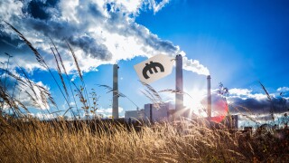 Concept: price tag for co2 emissions. Carbon tax. Composite image of a pricetag with a Euro sign attached to funnel of thermal power plant. Fumes emitted. Weed in the foreground, sun flares.