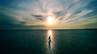 Little white boat floating on the water towards the horizon in t