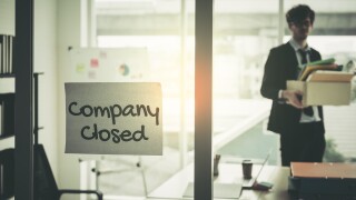 Company closed on windows of an empty office with business man packing beloning walking out of business by economic recession concept.