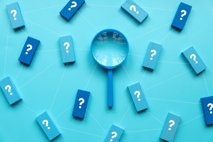 QnA or questions and answers concept. Blue magnifying glass with question symbol on wooden cube over a blue background.
