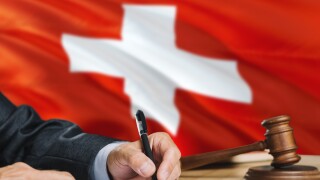 Judge writing on paper in courtroom with Switzerland flag background. Wooden gavel of equality theme and legal concept.