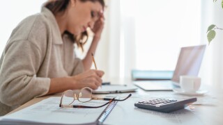 Eyeglasses and calculator close-up and tired accountant woman making marks in paper documents with modern laptop sitting background next bright daylight window. Business, home finances money savings
