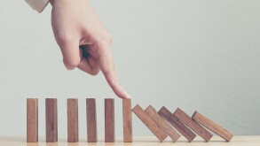 Hand stopping wooden domino business crisis effect or risk protection concept