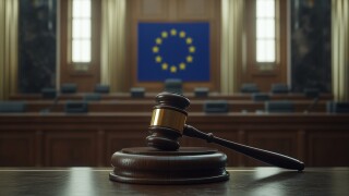 Judge's gavel is on a podium in front of a flag. The flag is a mix of European flags