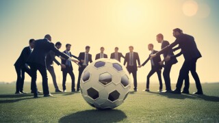 Businessmen in suits huddling around a soccer ball on a field