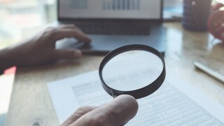 Business man using magnifying to review balance sheet annual with using  laptop computer to calculating budget. audit and Check integrity before investment concept.