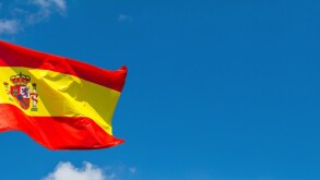 Flag of Spain waving in the wind on flagpole against the sky with clouds on sunny day, banner