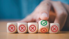 Hand flipping wooden cube block to change red cross mark to corr