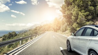A white car rushing along a high-speed highway in the sun.