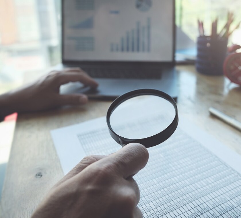 Business man using magnifying to review balance sheet annual with using  laptop computer to calculating budget. audit and Check integrity before investment concept.
