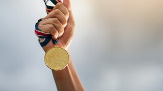 Hand holding gold medal on sky background