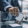 A close up of shareholders hand casting vote in transparent ballot box, showcasing importance of participation in decision making.