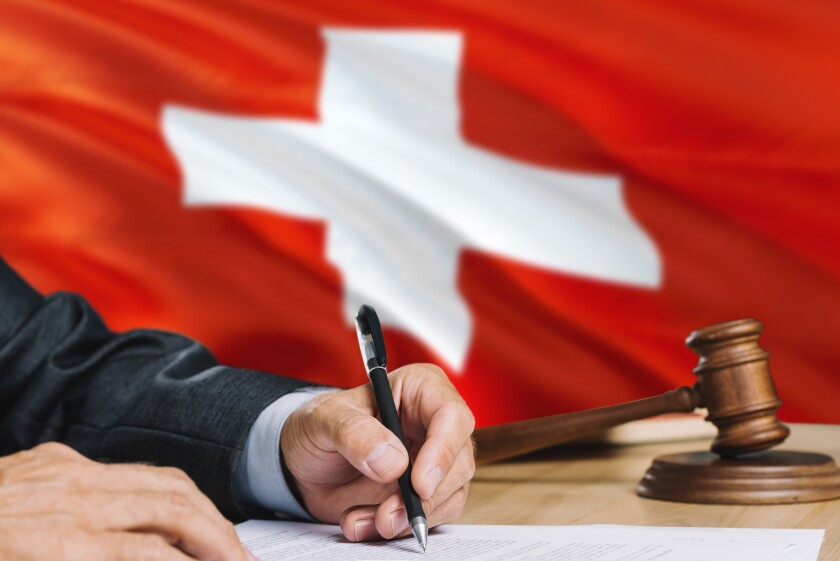 Judge writing on paper in courtroom with Switzerland flag background. Wooden gavel of equality theme and legal concept.
