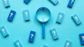 QnA or questions and answers concept. Blue magnifying glass with question symbol on wooden cube over a blue background.