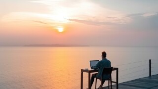 Man working remotely with his laptop from luxury location with the beautiful view on the sunset. He is enjoying the view on the sea. Created with generative AI