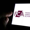 FCA Financial Conduct Authority logo on the smartphone and finger pointing at it in the dark room. Concept.  FCA is a financial regulatory body in the United Kingdom.