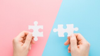 Young adult man and woman hands holding and putting together white puzzle pieces on light pink blue table background. Pastel color. Closeup. Concept of relationship compatibility. Top down view.